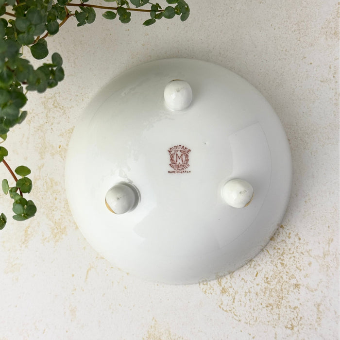 Underside of the white porcelain bowl showing three rounded feet and a red-brown Noritake maker's mark at the center.