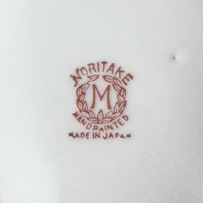 Close-up of the red-brown Noritake backstamp with a wreath surrounding the letter M and the words "Noritake," "Hand Painted," and "Made in Japan."
