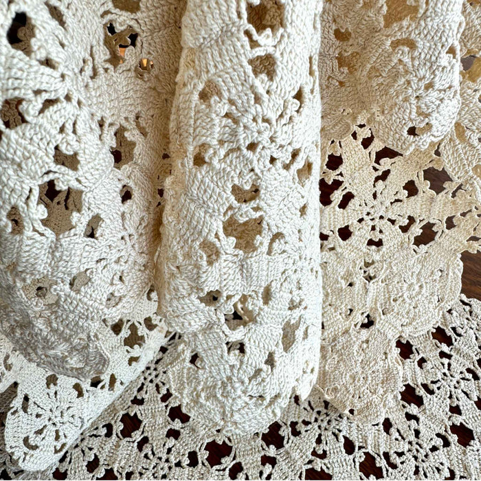 Close-up of the ecru crochet table runner draped in soft folds, showing the texture and openwork floral construction.