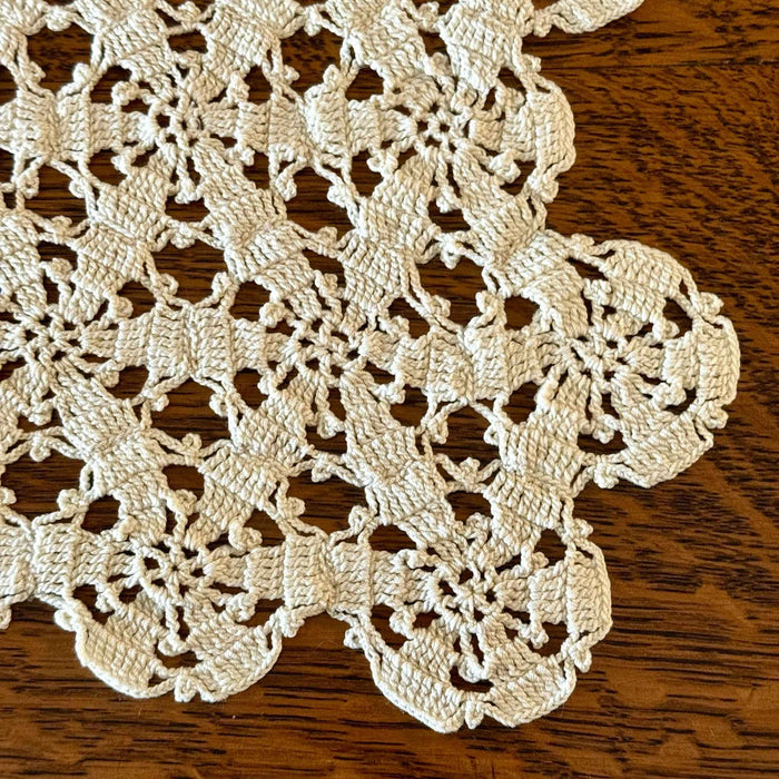 Close-up of a corner and scalloped edge of the ecru crochet table runner on a dark wood surface.