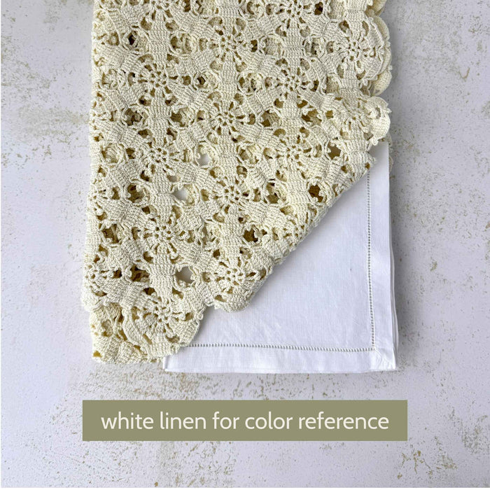 Ecru crochet table runner folded over a white linen textile for color comparison, showing the warmer color of the crochet.