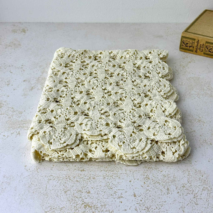 Neatly folded ecru crochet table runner showing the repeating floral openwork and scalloped edges.