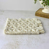Low-angle view of the folded ecru crochet table runner showing its soft, flexible layers and scalloped edge.