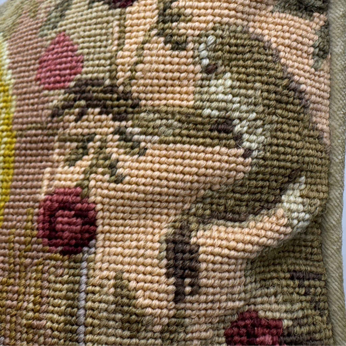 Detail of the wool needlepoint showing pink flowers, green foliage, and a small fanciful figure within the patterned background.