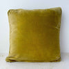 Back of the square pillow showing the solid rich tan velvet fabric and piped edges.