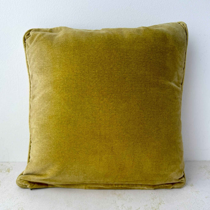 Back of the square pillow showing the solid rich tan velvet fabric and piped edges.