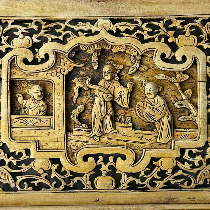 Close-up of central relief carving on vintage Chinese wood panel showing three robed figures in a courtyard scene with scrolling foliage in surrounding openwork
