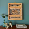 Vintage Chinese carved wood wall panel with openwork lattice surround and central relief scholar scene hanging on a blue-green wall with a plant, foo dog figurine, and calligraphy box on wood surface below