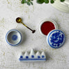 Close-up of vintage Chinese calligraphy water dropper, brass spoon, open porcelain seal paste container, and brush rest on a light surface