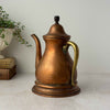 Vintage copper kettle with brass handle shown at a three-quarter angle, highlighting the curved body and aged copper patina.