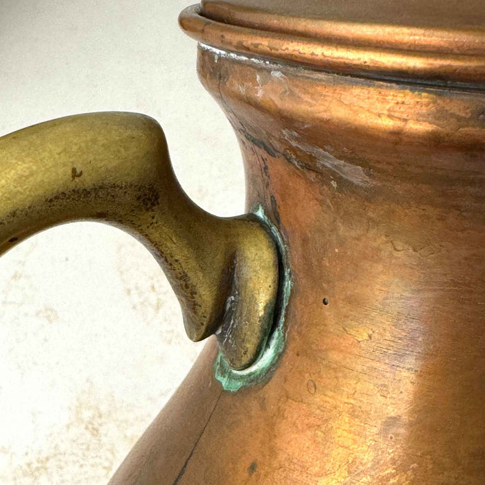 Close-up of the brass handle attachment on the vintage copper kettle, showing verdigris and surface wear.