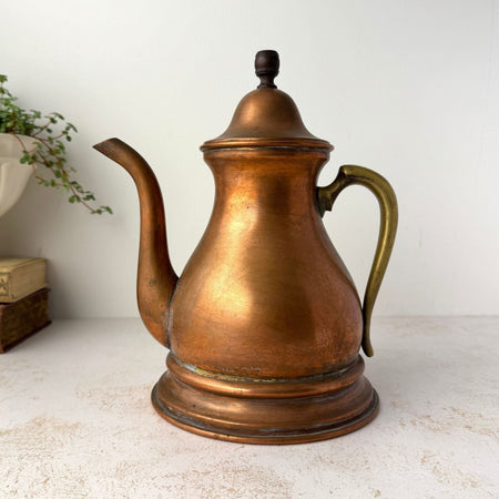 Vintage copper kettle with brass handle, long curved spout, domed lid, and warm aged patina.