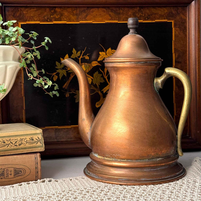 Vintage copper kettle with brass handle styled with antique books, greenery, and a decorative wood tray.