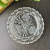 Overhead view of a round clear glass dish with three radiating flowers, pointed leaves, geometric star patterns, and a deeply notched rim.