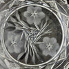 Close-up of three stylized flowers with finely radiating petals, pointed leaves, and a small geometric star at the center of the clear glass dish.