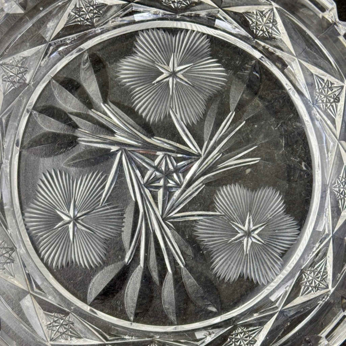 Close-up of three stylized flowers with finely radiating petals, pointed leaves, and a small geometric star at the center of the clear glass dish.