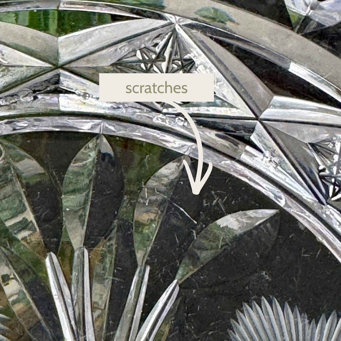 Extreme close-up of the glass dish showing fine surface scratches among the floral and geometric decoration.