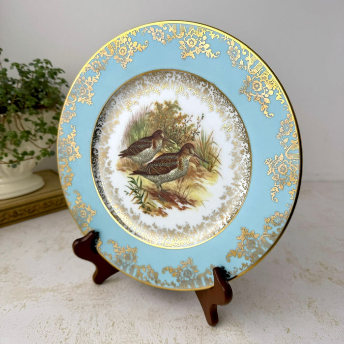 Vintage JKW porcelain game bird plate on a wooden stand, showing two snipe, a turquoise blue rim and ornate gold decoration.