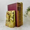 Pair of carved golden olive soapstone bookends holding antique clothbound books on a light textured surface