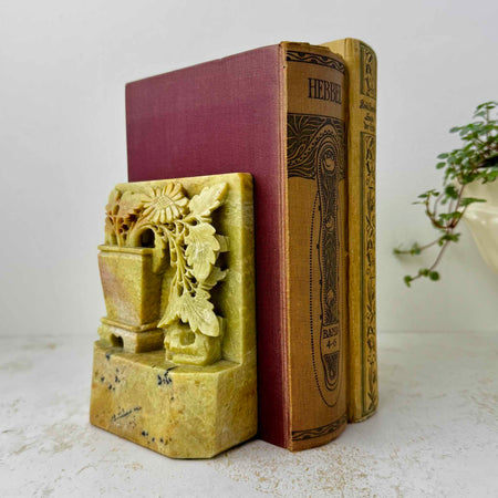 Pair of carved golden olive soapstone bookends holding antique clothbound books on a light textured surface