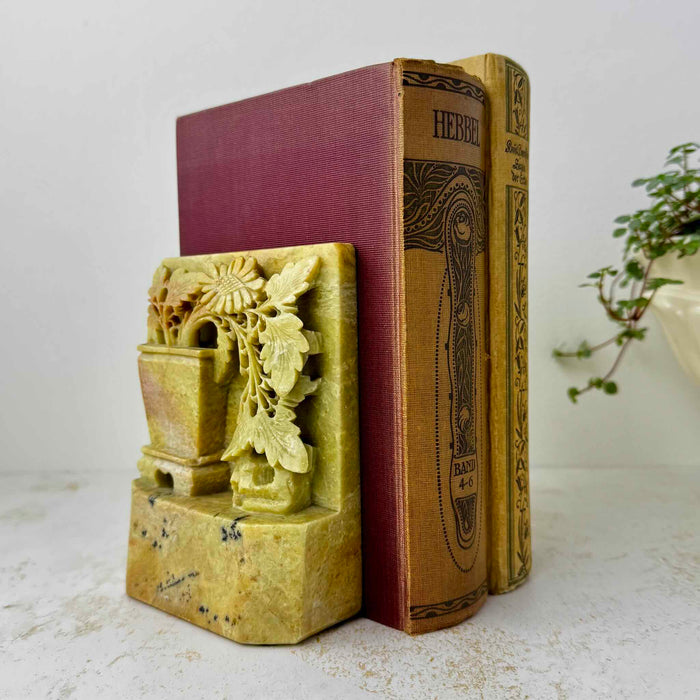 Pair of carved golden olive soapstone bookends holding antique clothbound books on a light textured surface