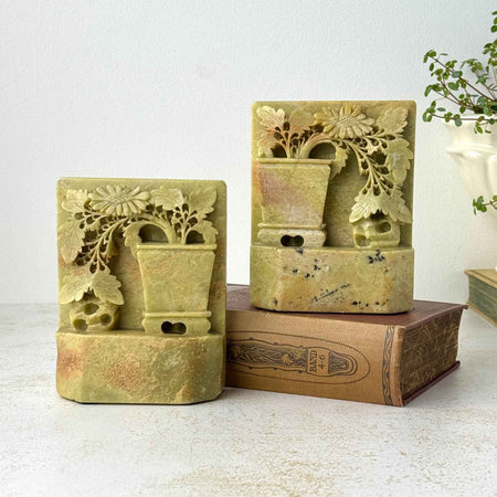Pair of carved soapstone bookends displayed with books, showing dimensional potted plants, flowers and natural stone variation