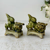Pair of vintage green glazed foo dogs or guardian lion figures displayed on a textured off-white surface against a neutral background