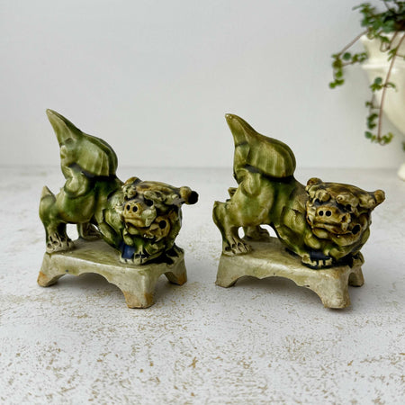 Pair of vintage green glazed foo dogs or guardian lion figures displayed on a textured off-white surface against a neutral background