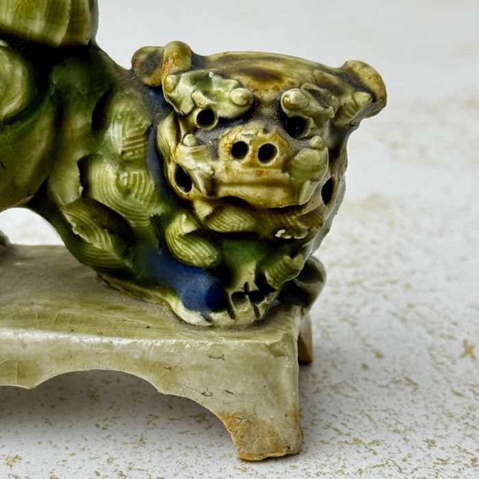 Close-up detail of a vintage green glazed foo dog figure showing the expressive face, textured carving, and mottled glaze