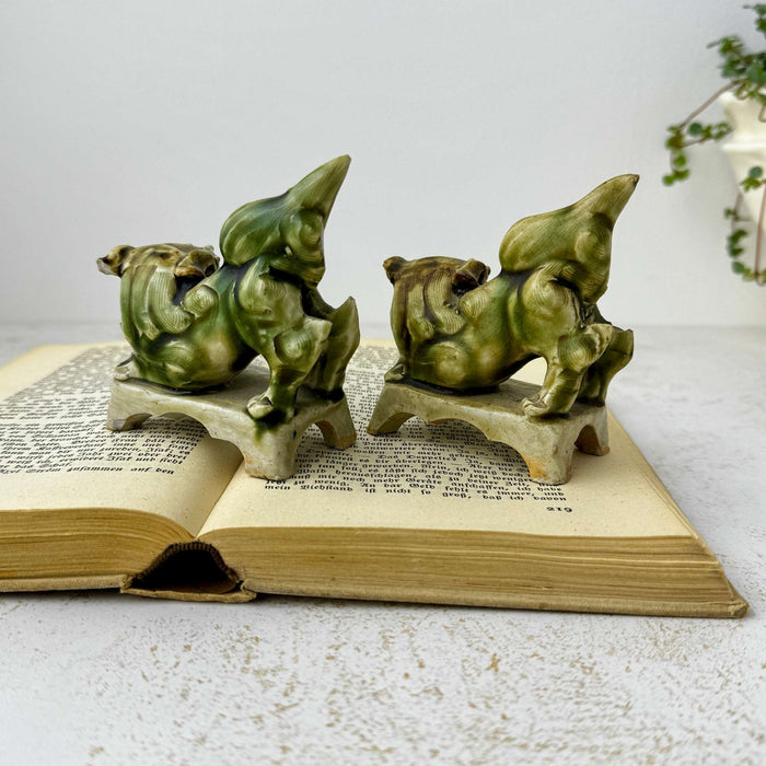 Rear view of a pair of vintage green glazed foo dog figures displayed on an open antique book