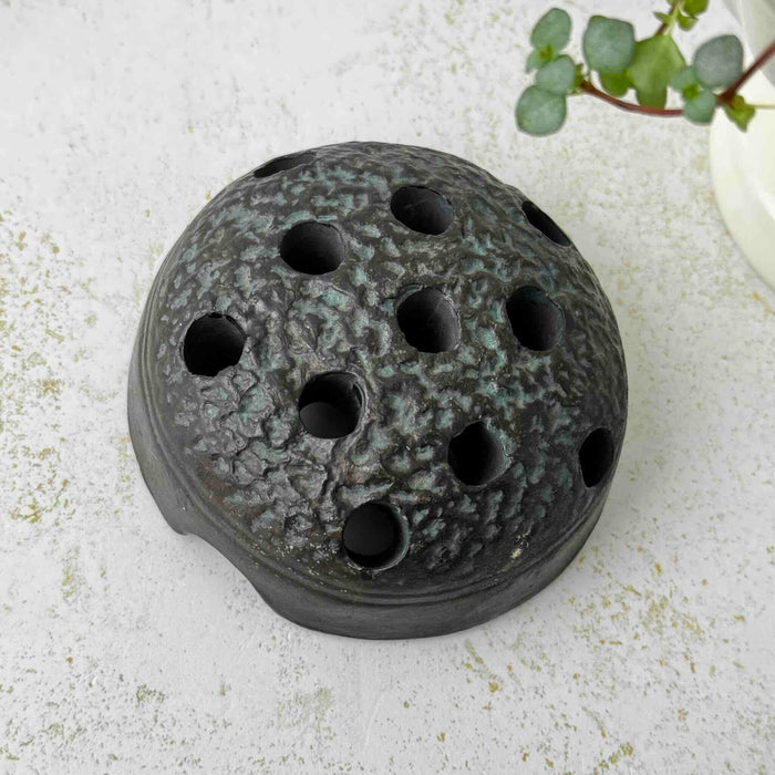Vintage Japanese ceramic flower frog with an organic domed form and dark earthy glaze on a light surface