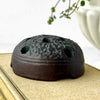 Side view of vintage Japanese ceramic flower frog with an organic domed form and dark earthy glaze on a closed antique book
