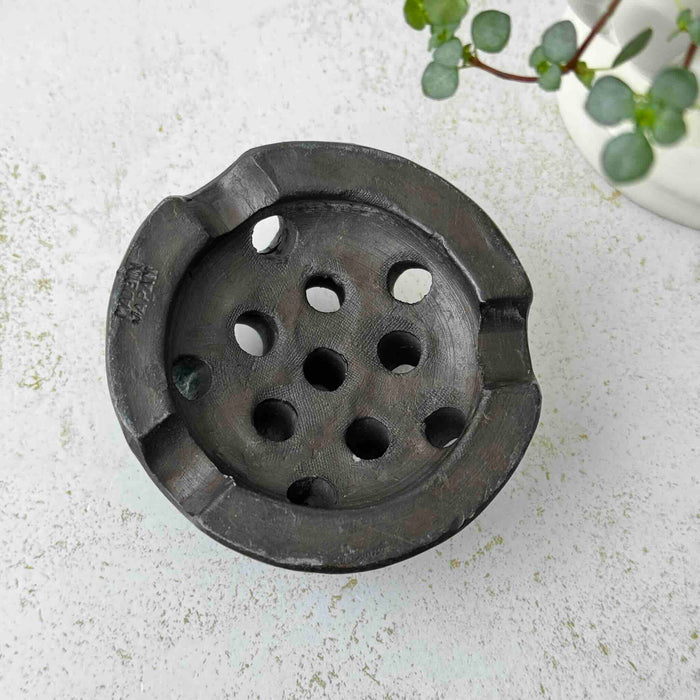 Undersie of vintage Japanese ceramic flower frog with an organic domed form and dark earthy glaze on a light surface
