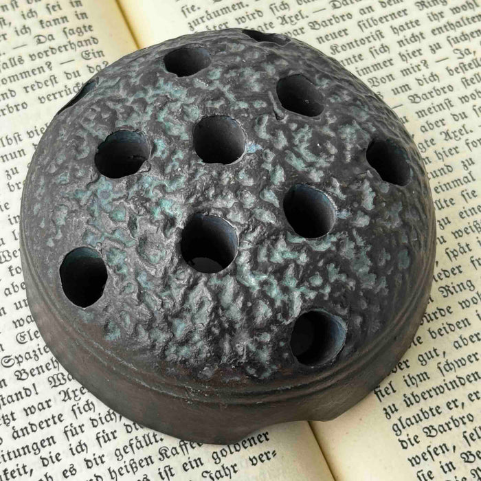 Close-up of vintage Japanese ceramic flower frog with an organic domed form and dark earthy glaze resting on an open antique book