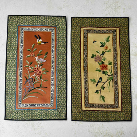 Pair of vintage Chinese embroidered textile wall panels with bird and floral motifs on rust and pale gold backgrounds, bordered with patterned green fabric