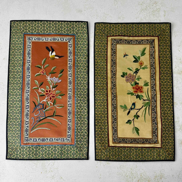 Pair of vintage Chinese embroidered textile wall panels with bird and floral motifs on rust and pale gold backgrounds, bordered with patterned green fabric
