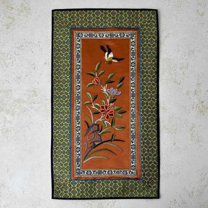Vintage Chinese embroidered wall hanging with bird and floral design on a rust-colored textile panel with patterned green border