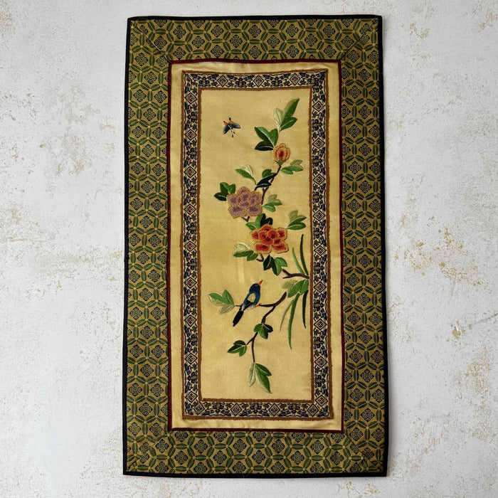 Vintage Chinese embroidered wall hanging with floral branches and birds on a pale gold textile panel with patterned green border