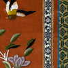 Close-up of vintage Chinese embroidery showing bird, floral motif, patterned trim, and textured stitching on rust-colored fabric panel