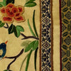 Close-up of vintage Chinese embroidery showing floral branch, bird, patterned trim, and textured stitching on pale gold fabric panel