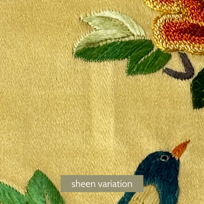 Close-up of vintage Chinese embroidered textile panel showing a small area of sheen variation on pale gold fabric near embroidered floral and bird motifs