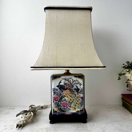 Vintage chinoiserie-style peacock accent lamp with original cream shade, featuring colorful peacocks, peonies, and navy and gold detailing on a dark wood base