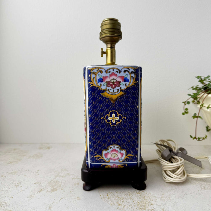Side view of a vintage ceramic peacock lamp showing navy and gold floral side decoration and wood base