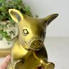 Close-up front view of one brass pig bookend showing its pointed ears, snout, engraved facial details, and raised hooves.