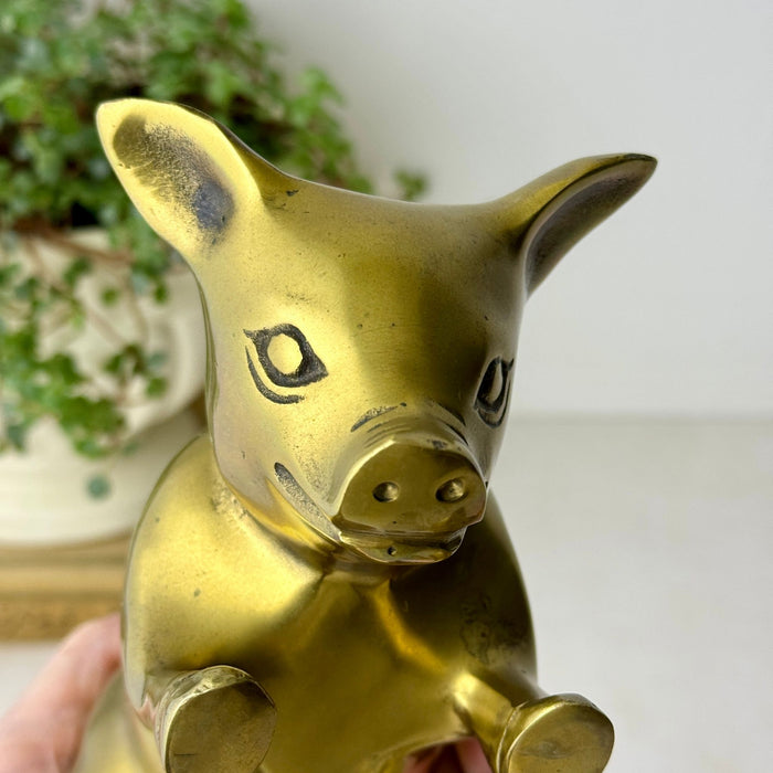 Close-up front view of one brass pig bookend showing its pointed ears, snout, engraved facial details, and raised hooves.