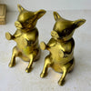 Angled front view of the pair of brass pig bookends showing their expressive faces, raised hooves, and seated bodies.