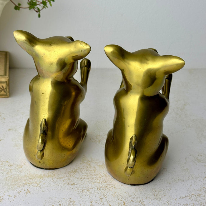 Rear view of the vintage brass pig bookends showing their rounded backs and curled tails.