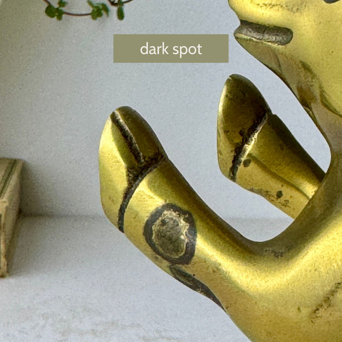 Close-up of a dark spot on the front leg of one vintage brass pig bookend.