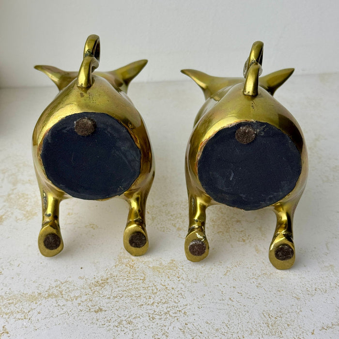 Underside view of both vintage brass pig bookends showing black felt-covered bases and small felt pads.