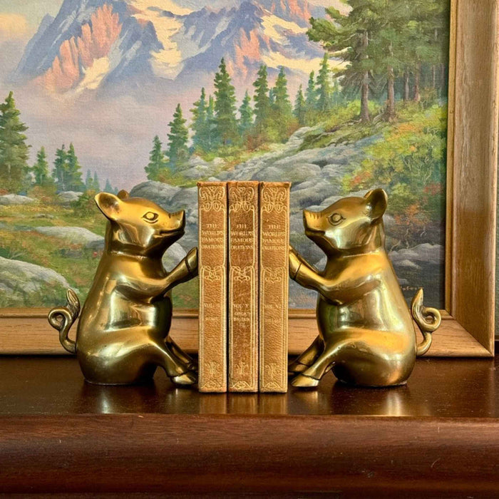 Pair of vintage brass pig bookends facing each other with three small books between them on a wooden shelf.